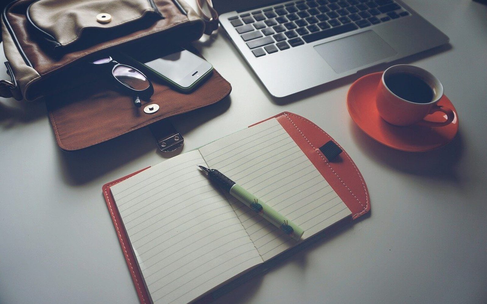 Carnet, stylo, ordinateur et café posés sur un bureau